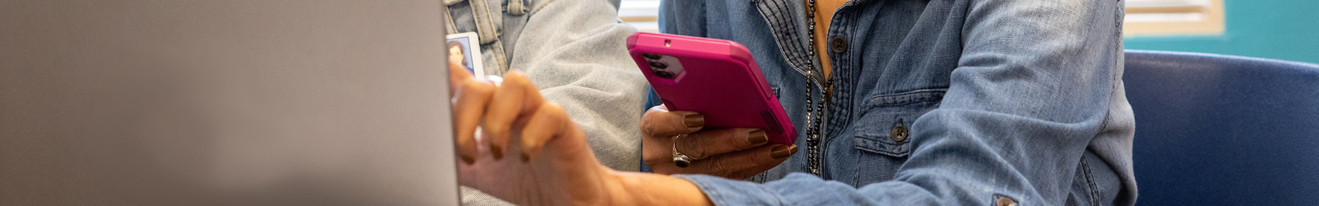 Person sitting behind a laptop with one hand pointing toward the screen and the other holding a phone