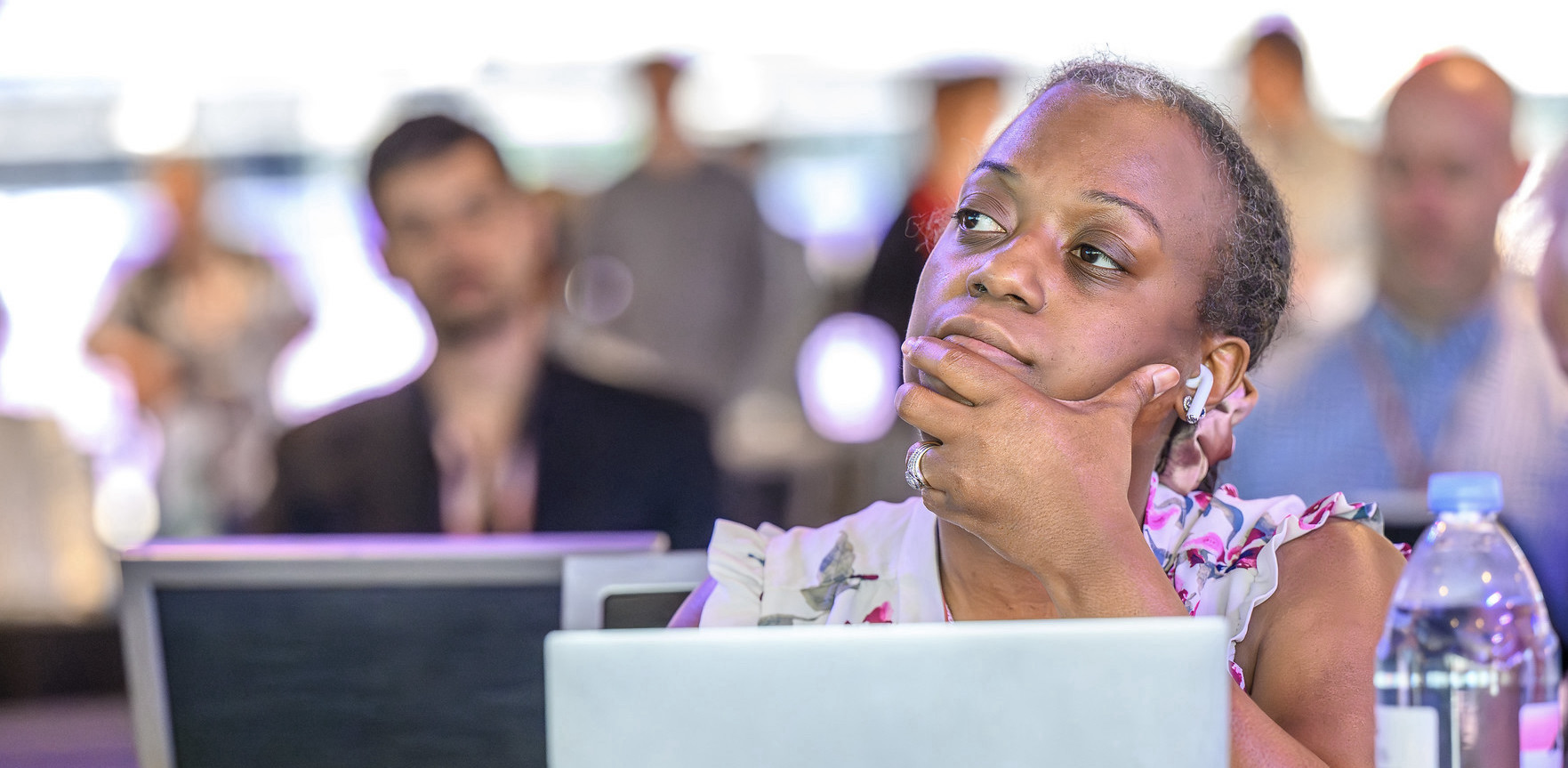 Woman sitting behind a laptop listening to someone out of frame with her hand wrapped around her jaw and chin