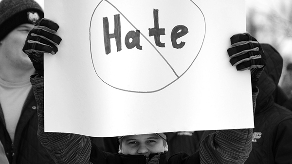 Person holding a sign with the word hate with a circle and a slash drawn around it