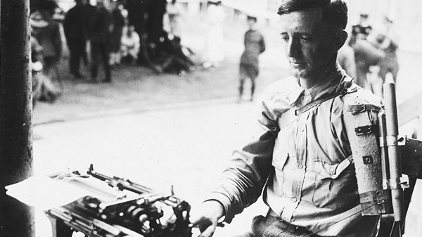 Man with one arm wearing a military uniform and typing on a typewriter with his hand