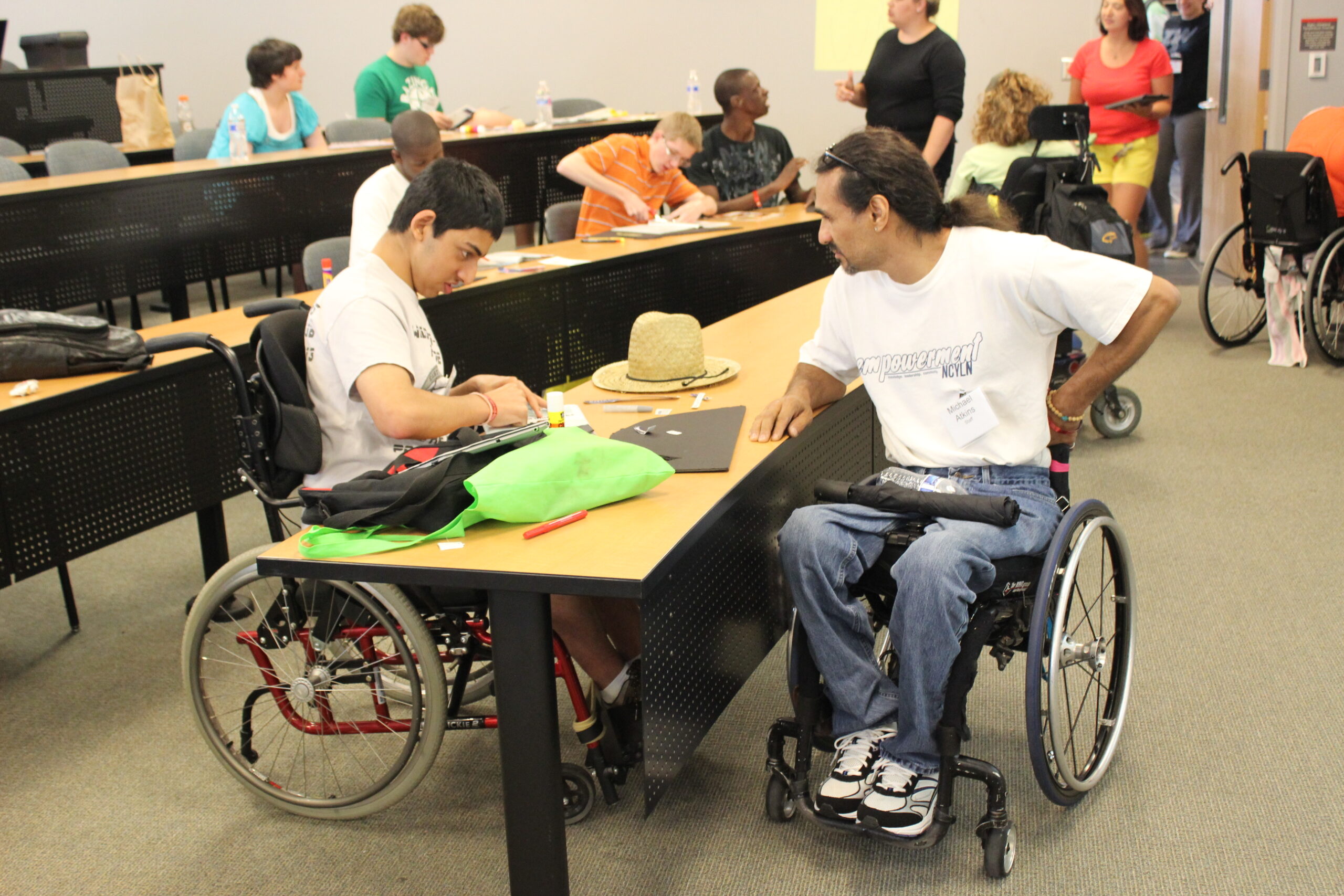 Two wheelchair users talk at a table during a classroom activity.