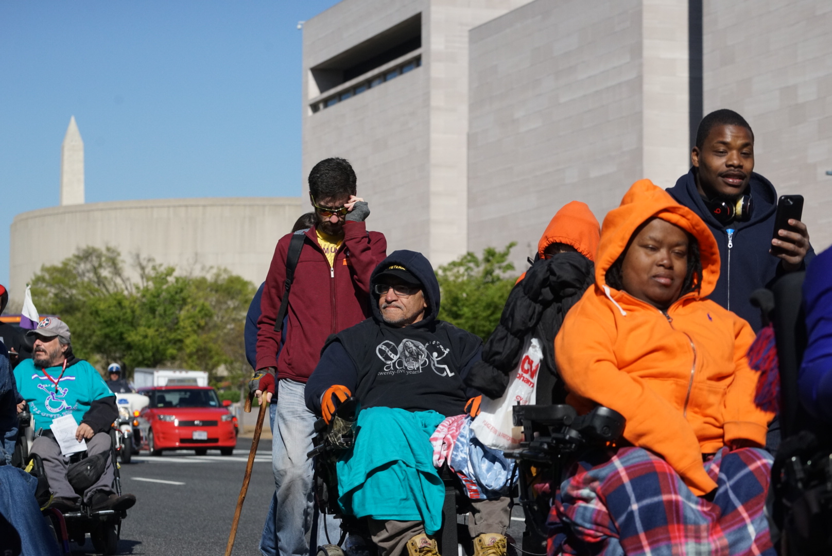 People, several using wheelchairs, move together along a city street.