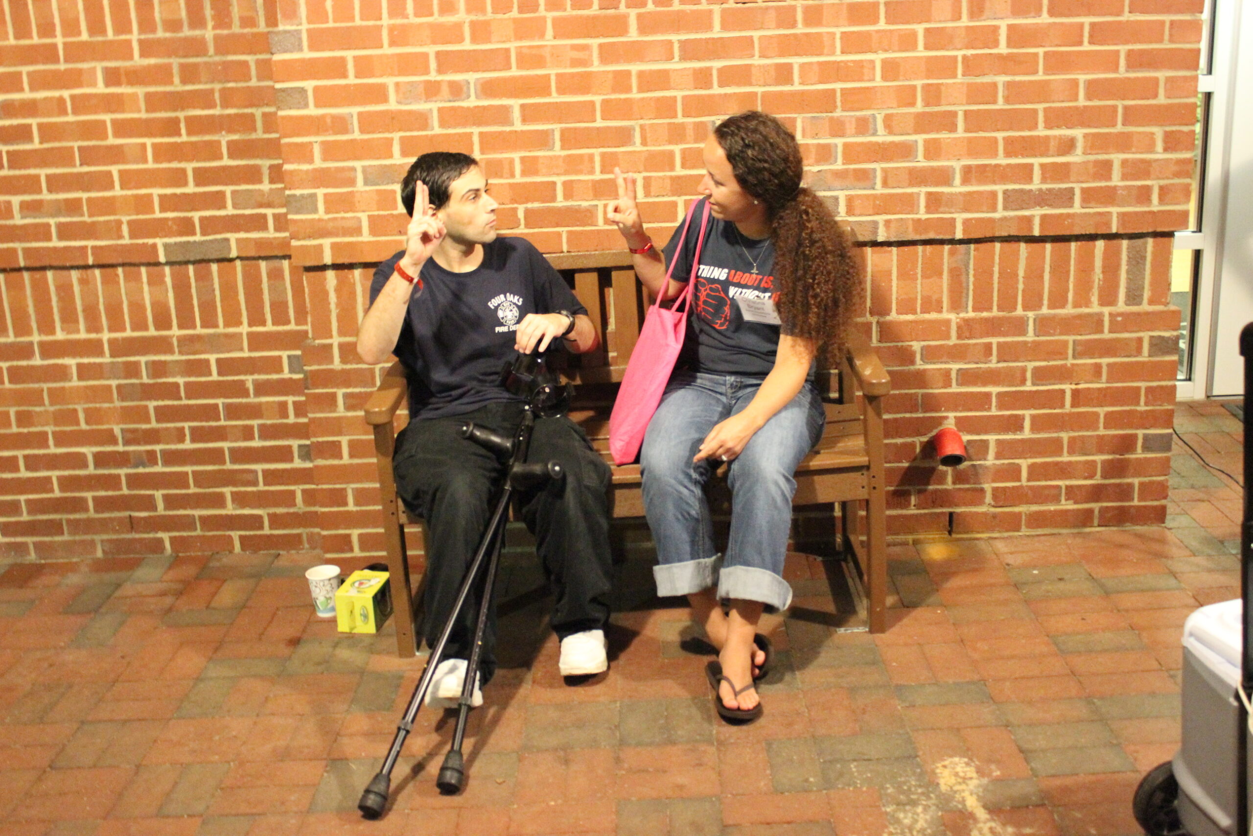 Two people sit on a bench, using hand signs while talking.