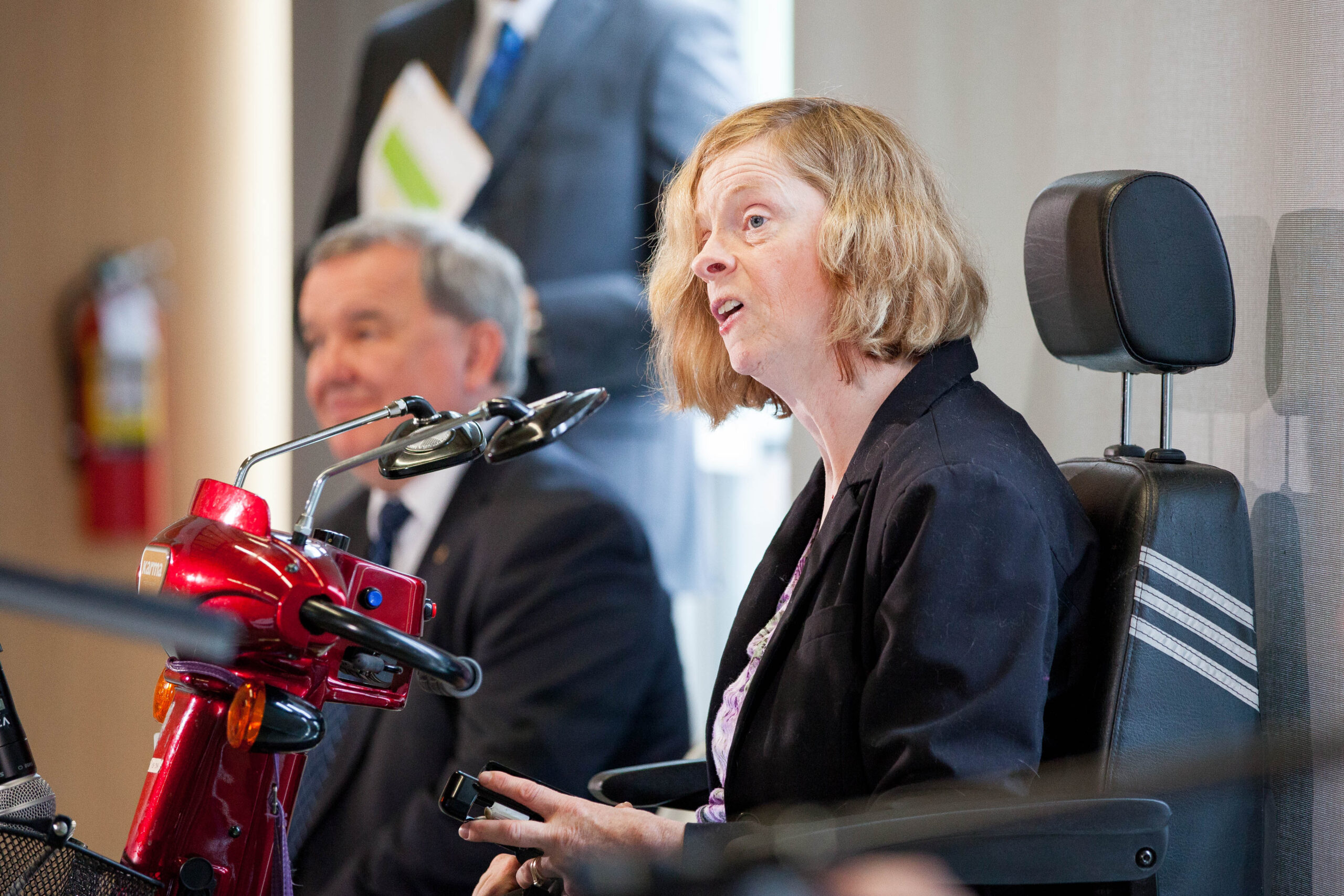 Woman using a red mobility scooter speaks into a microphone.