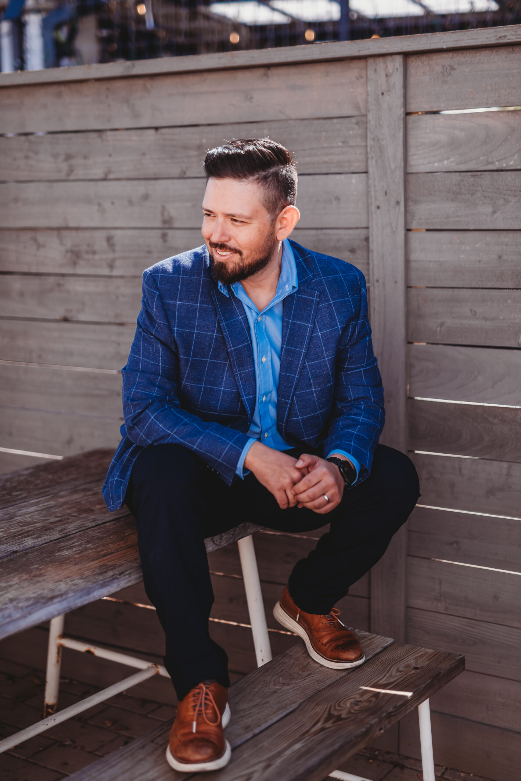 Joey Vega sits on top of a picnic table in professional dress and looks to his left with a smile on his face.