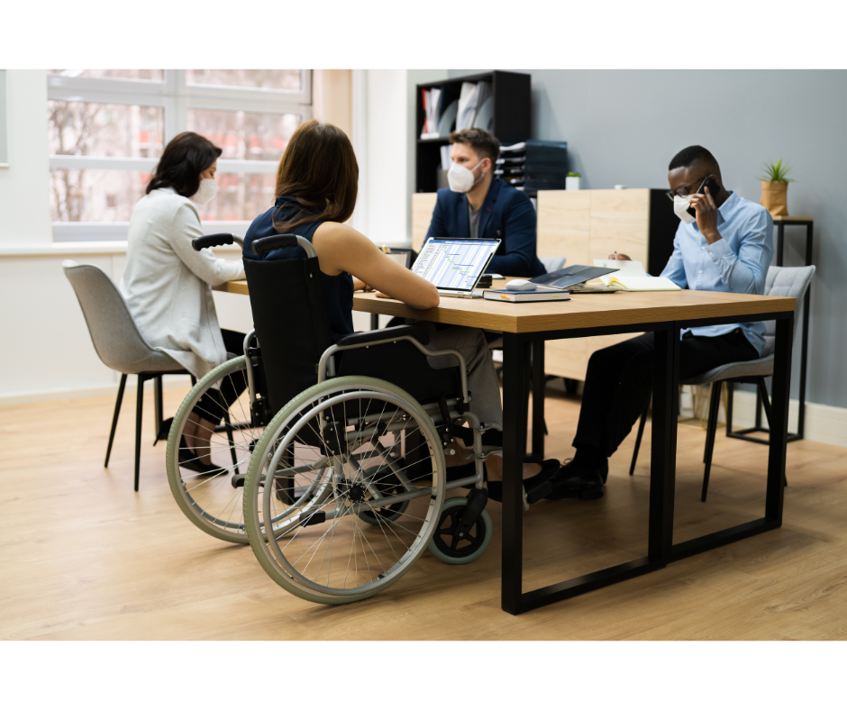 Diverse group in a meeting room, including a person in a wheelchair, collaborating around a table.