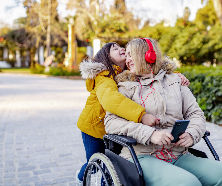 Child hugging a smiling adult in a wheelchair outdoors.