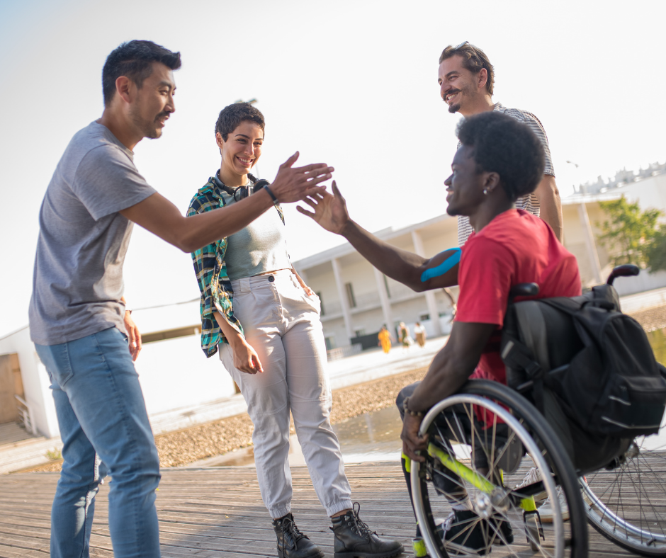Friends greeting a wheelchair user with a high five outside.