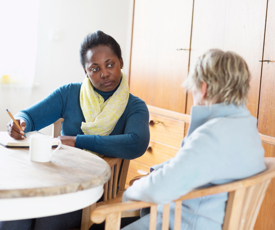 Two people in discussion at a table, one taking notes during a meeting.