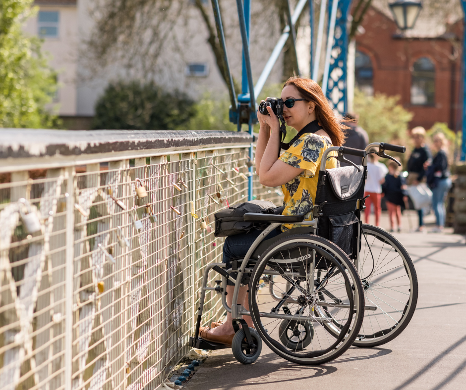 Wheelchair user taking a photo on a bridge.