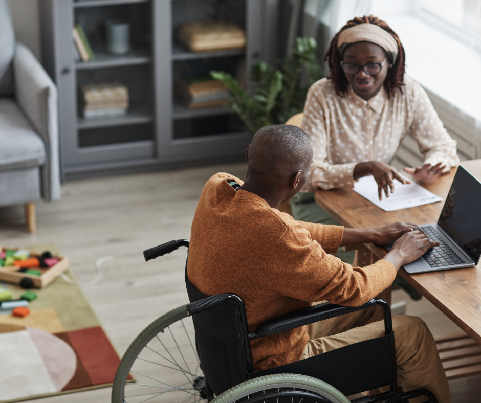 Service provider meeting with a wheelchair user at a laptop.