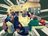 A photo showing staff members sitting around a table and engaging in lively discussion. Some staff use wheelchairs.