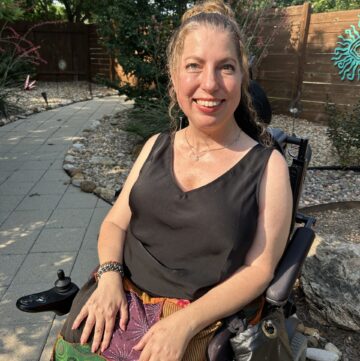 Emily Wolinsky sitting in her power wheelchair in an outdoor garden.